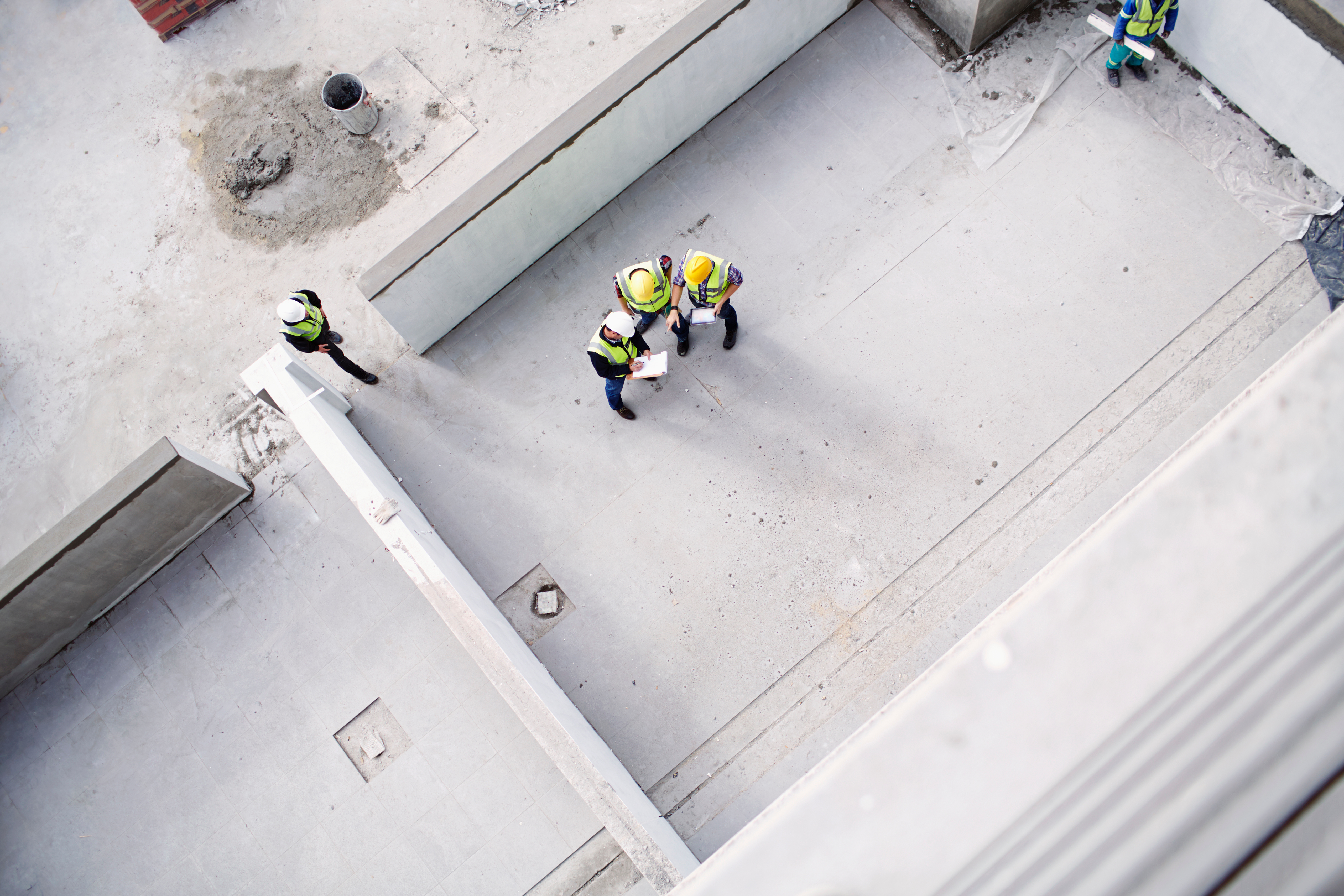 Aerial view of construction workers wearing safety gear and helmets, discussing plans on a concrete site