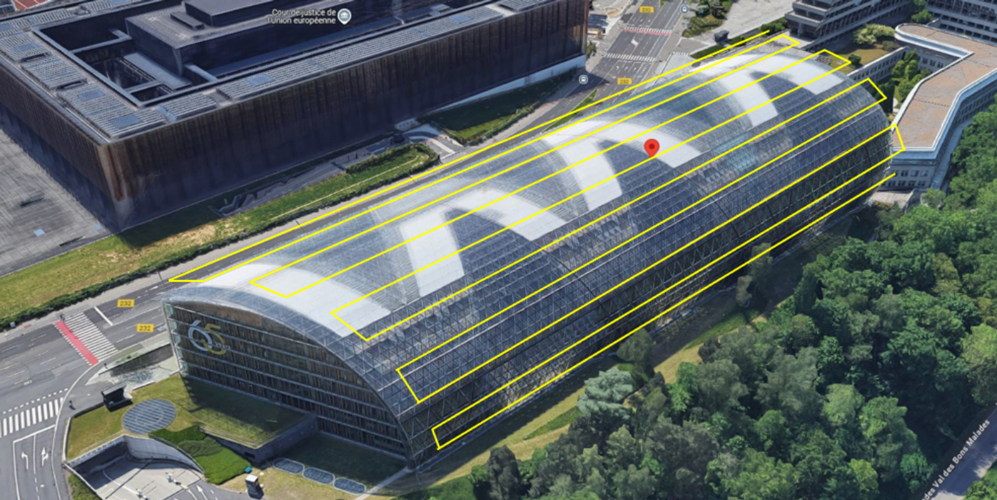 Aerial view of a modern glass-roofed building, part of the European Court of Justice complex in Luxembourg, surrounded by trees and adjacent roads