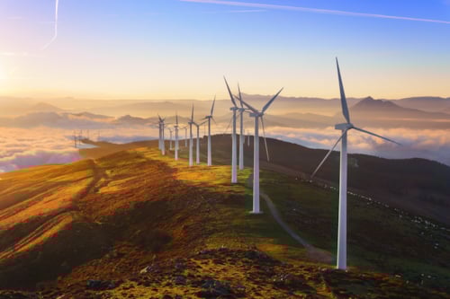 Kiwa inspected wind turbines on a hilltop at sunrise with a scenic view of mountains and clouds in the background