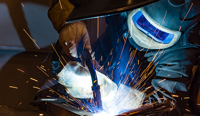 Svetsare lutar lite åt sidan medan han svetsar. Svetslågor sprutar upp.