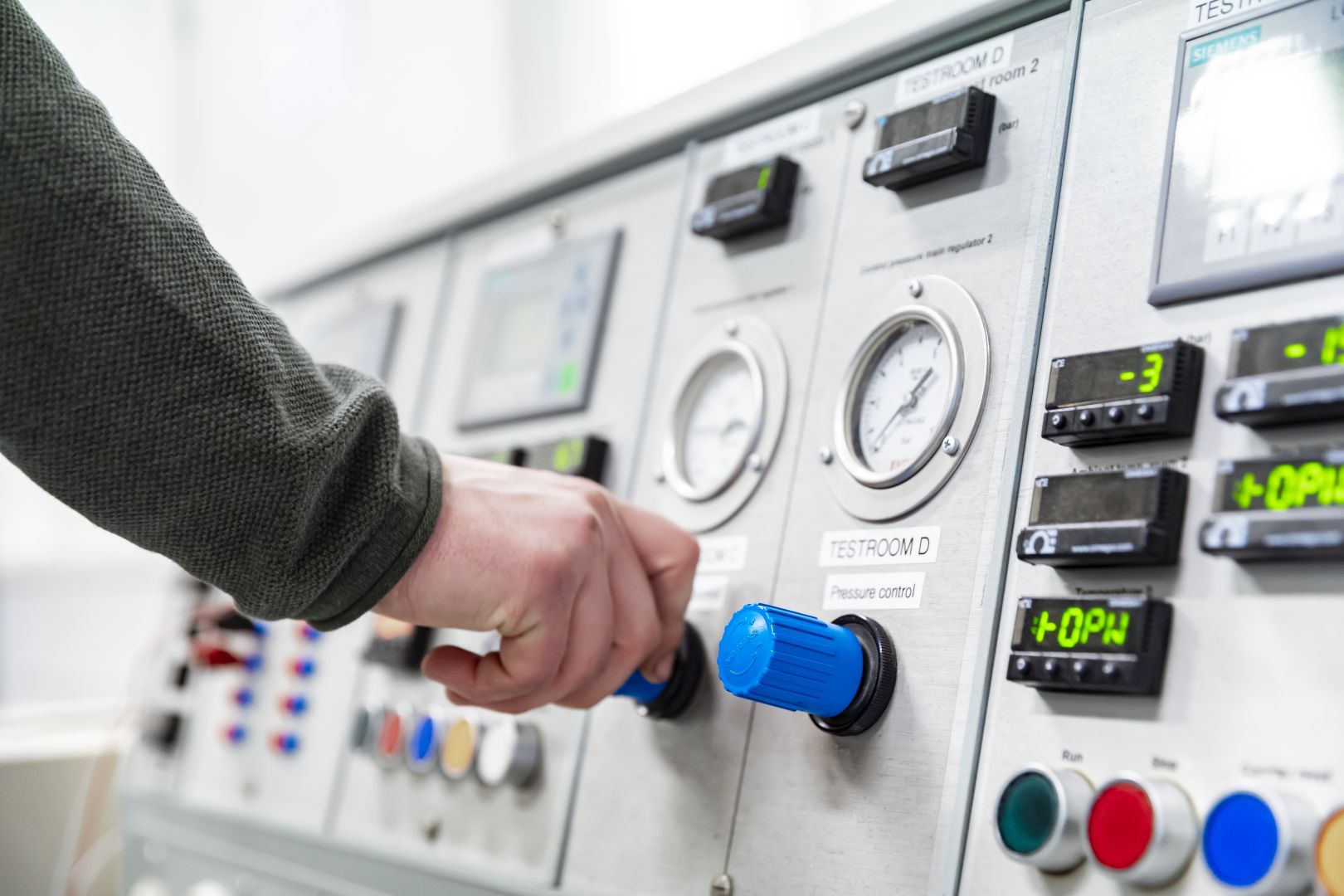 Person adjusting control knobs on an industrial pressure monitoring panel displaying gauges and digital readings