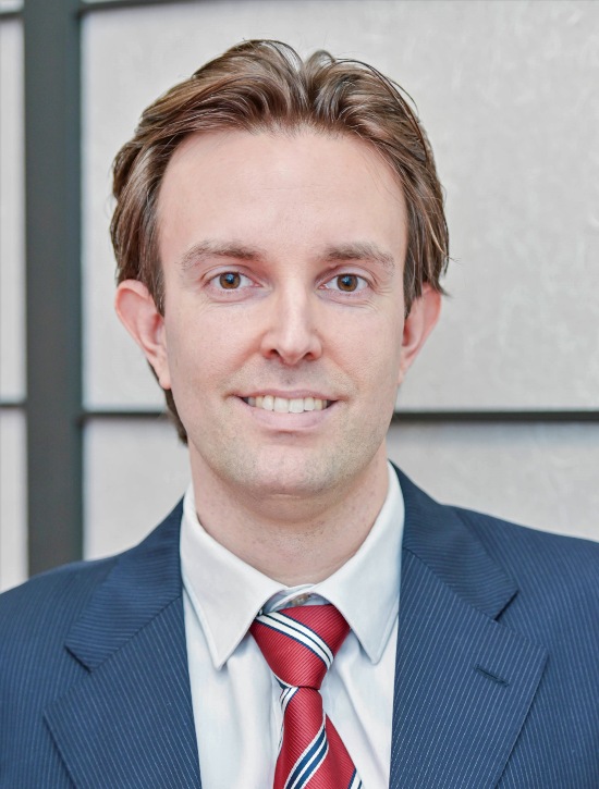 Luca Votta in a suit and red tie smiling in a corporate setting