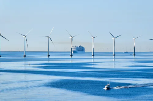 A Kiwa certified offshore wind farm with multiple turbines in calm blue waters, featuring a cruise ship in the background and a small boat in the foreground