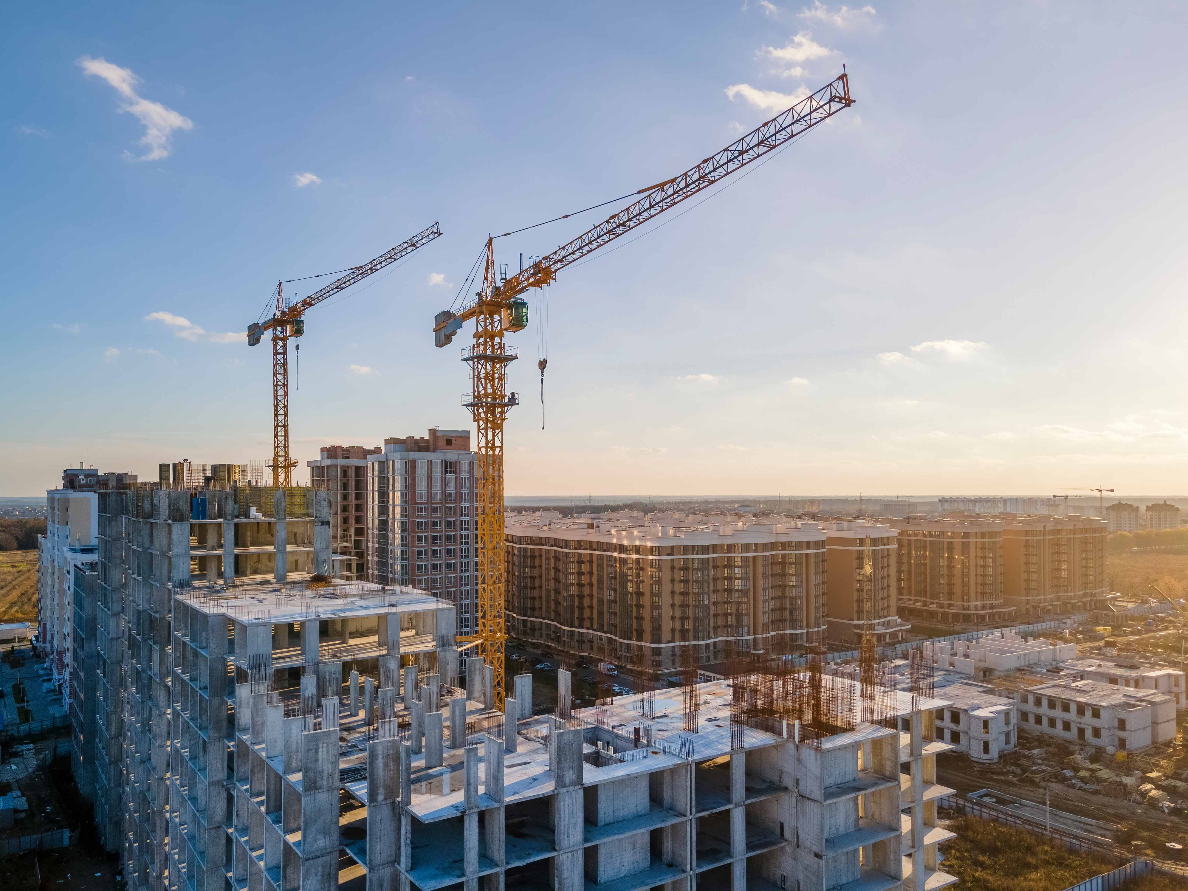 Construction site with cranes and partially built high-rise buildings under a clear sky, showcasing urban development and progress