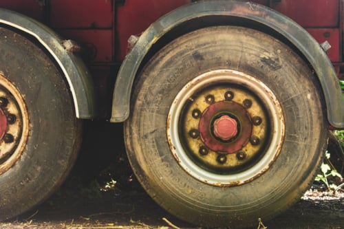 Close-up of two truck wheels with worn tires and red rims parked on a dirt surface
