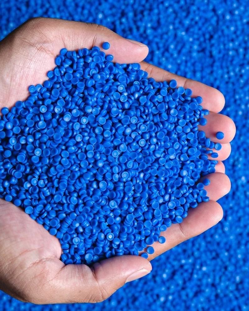 Hands holding a pile of Kiwa tested blue plastic pellets, used for industrial manufacturing and recycling processes