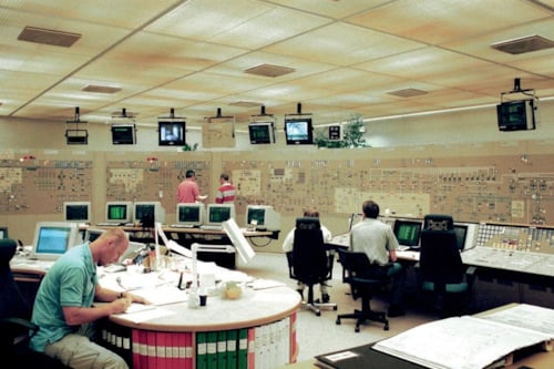 Control room with multiple operators working at desks, surrounded by computer monitors and control panels, in a high-tech facility