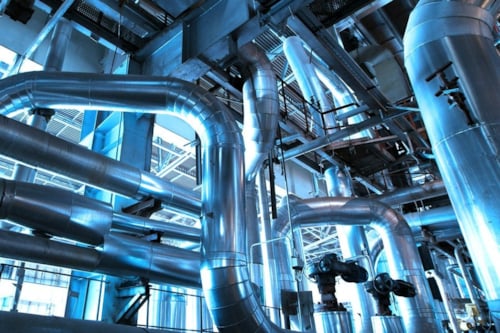 Industrial piping system with interconnected metal pipes and valves, showcasing complex engineering infrastructure within a facility, with a blue-tinted lighting
