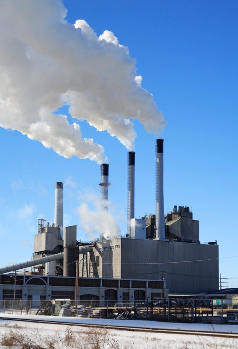 Industrial power plant with four smokestacks emitting white smoke against a clear blue sky