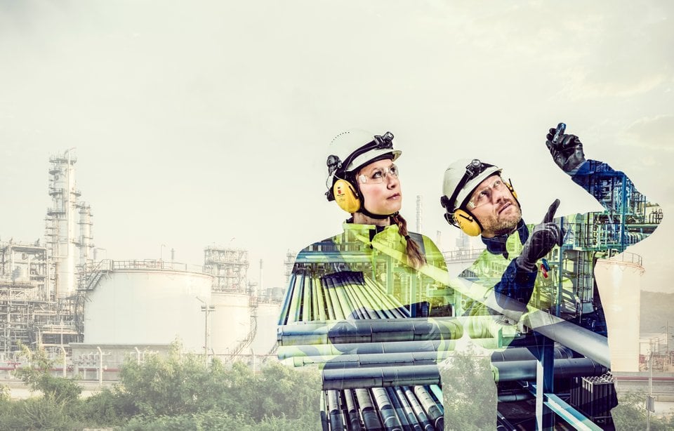 Industrial engineers wearing safety gear and helmets, examining processes at a petrochemical plant with industrial equipment and storage tanks in the background