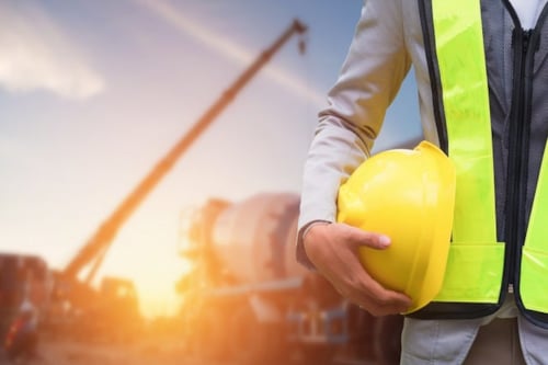 close-up of a man holding a helmet in a construction site during the golden hour