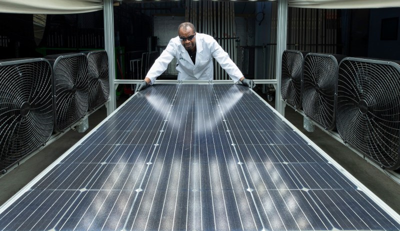 Kiwa laboratory employee in a lab coat inspecting a large solar panel surrounded by industrial fans in a testing facility