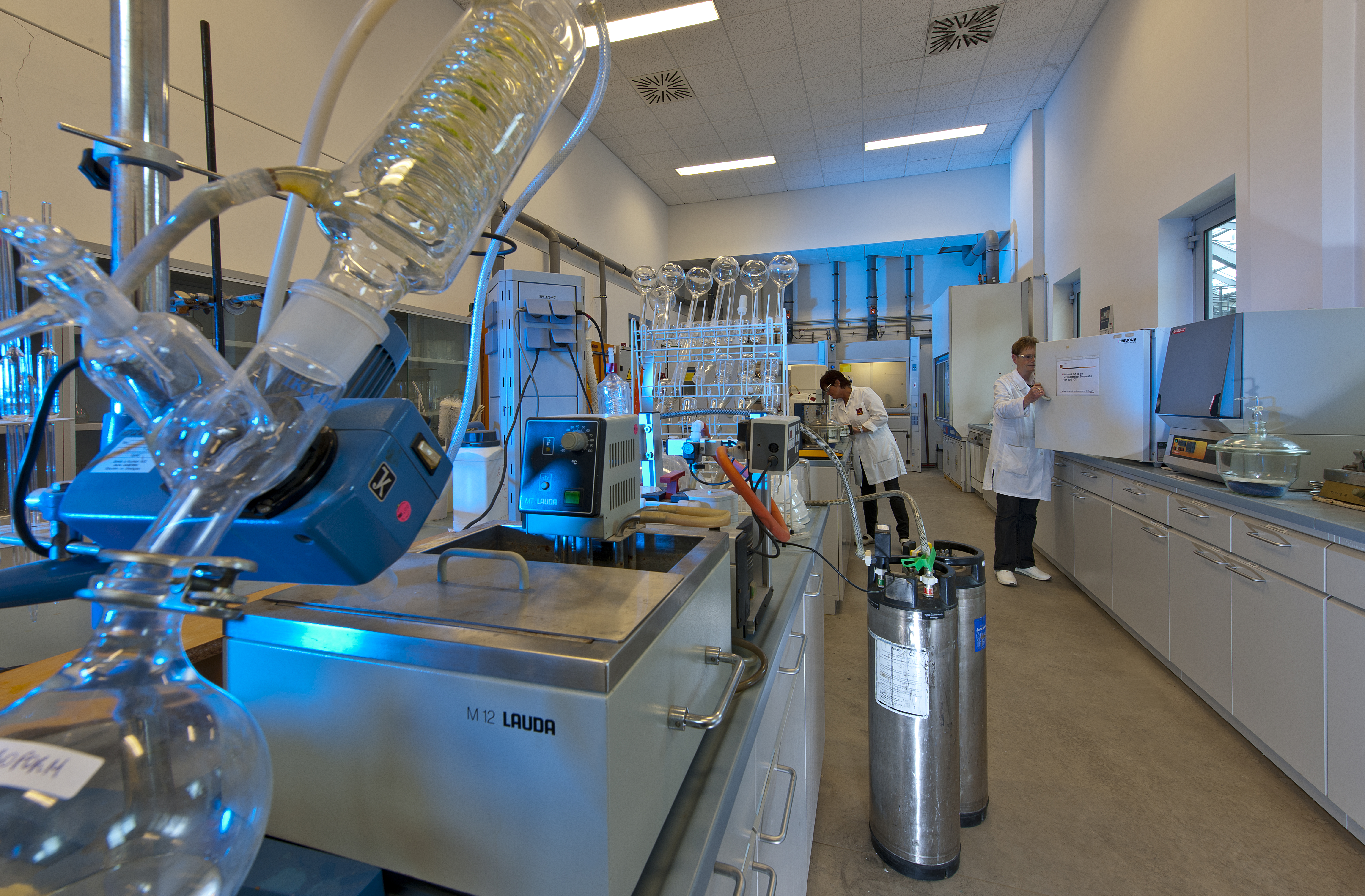 Modern chemistry laboratory with advanced equipment and Kiwa laboratory employees conducting experiments. The lab features distillation apparatus and storage tanks, showcasing a professional research environment