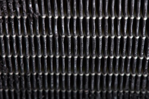 Close-up of industrial woven metallic mesh with vertical and horizontal black threads forming a grid pattern