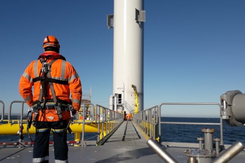 man standing in a platform of a standing windmill, to conduct a non-destructive test on the wind power asset