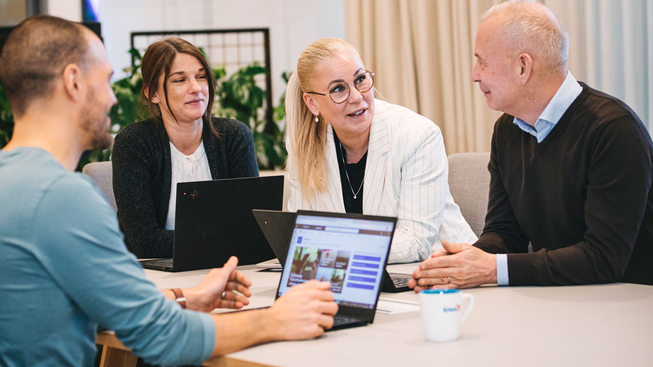 Deltagare sitter med varsin laptop och pratar runt ett bord. 