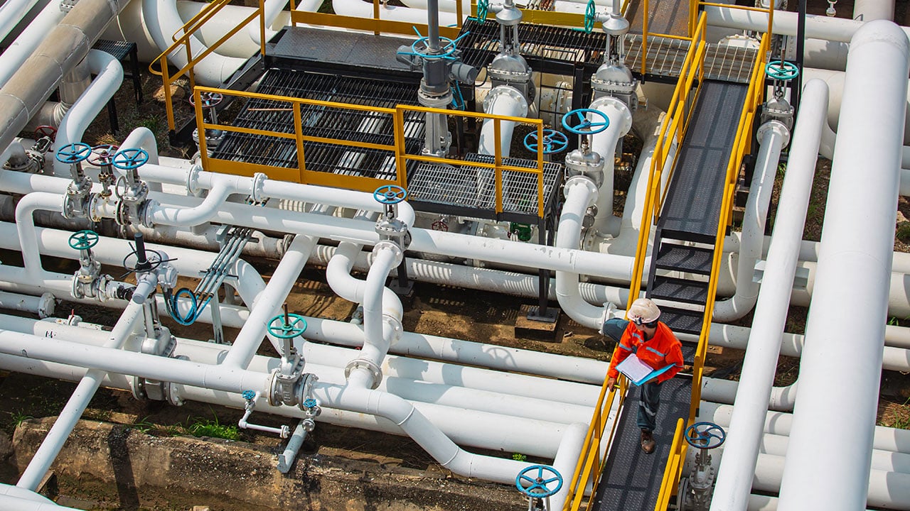 Tekniker inspekterar utomhus ventiler och rörledningar i en industri.
