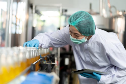A Kiwa inspector wearing protective gear inspects glass bottles in a beverage production line