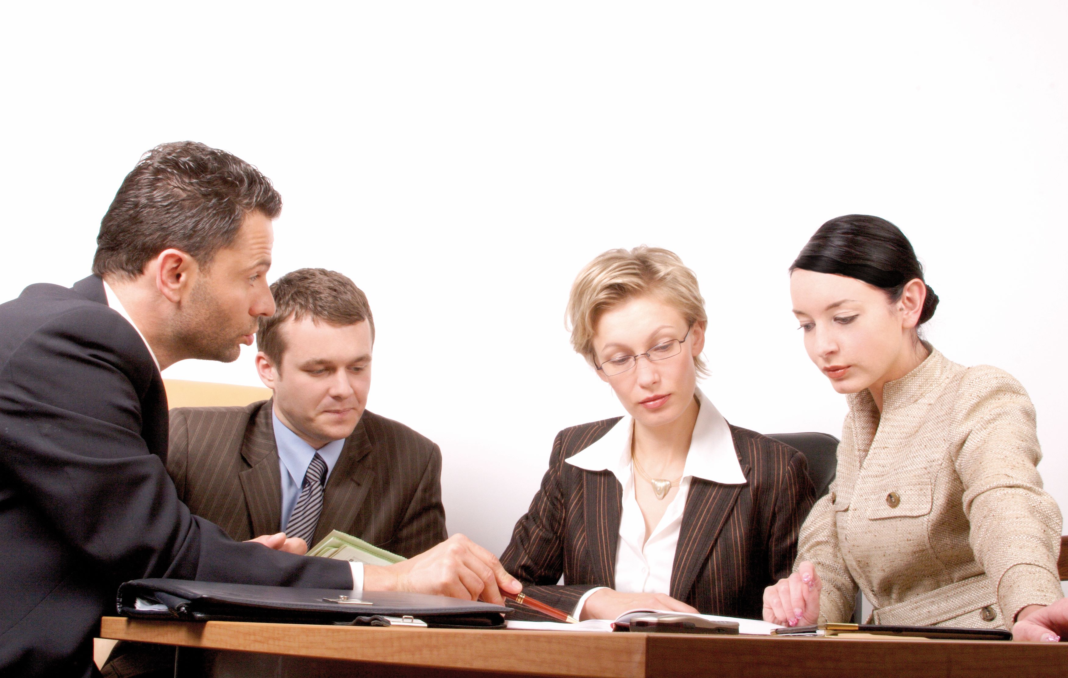 Group of four business professionals engaged in a meeting at a conference table, focused on documents