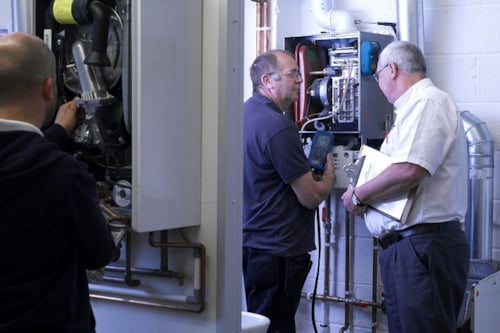 Kiwa trainer and student servicing and inspecting industrial boilers in a mechanical room during a class room course.