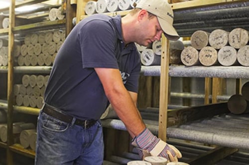 Kiwa employee examining geological core samples in a storage facility wearing casual attire and protective gloves