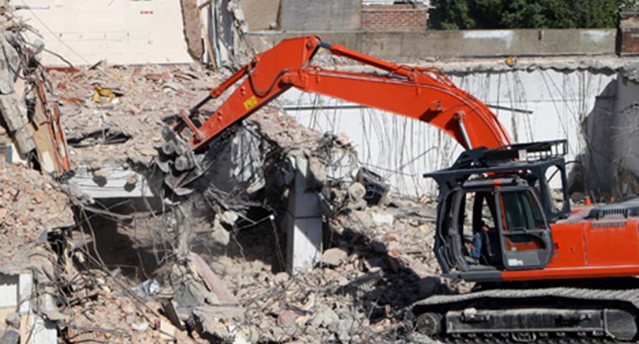 Excavator demolishing an old building structure amid debris