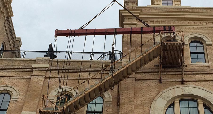 Old brick building facade with wooden outdoor staircase supported by a metal beam