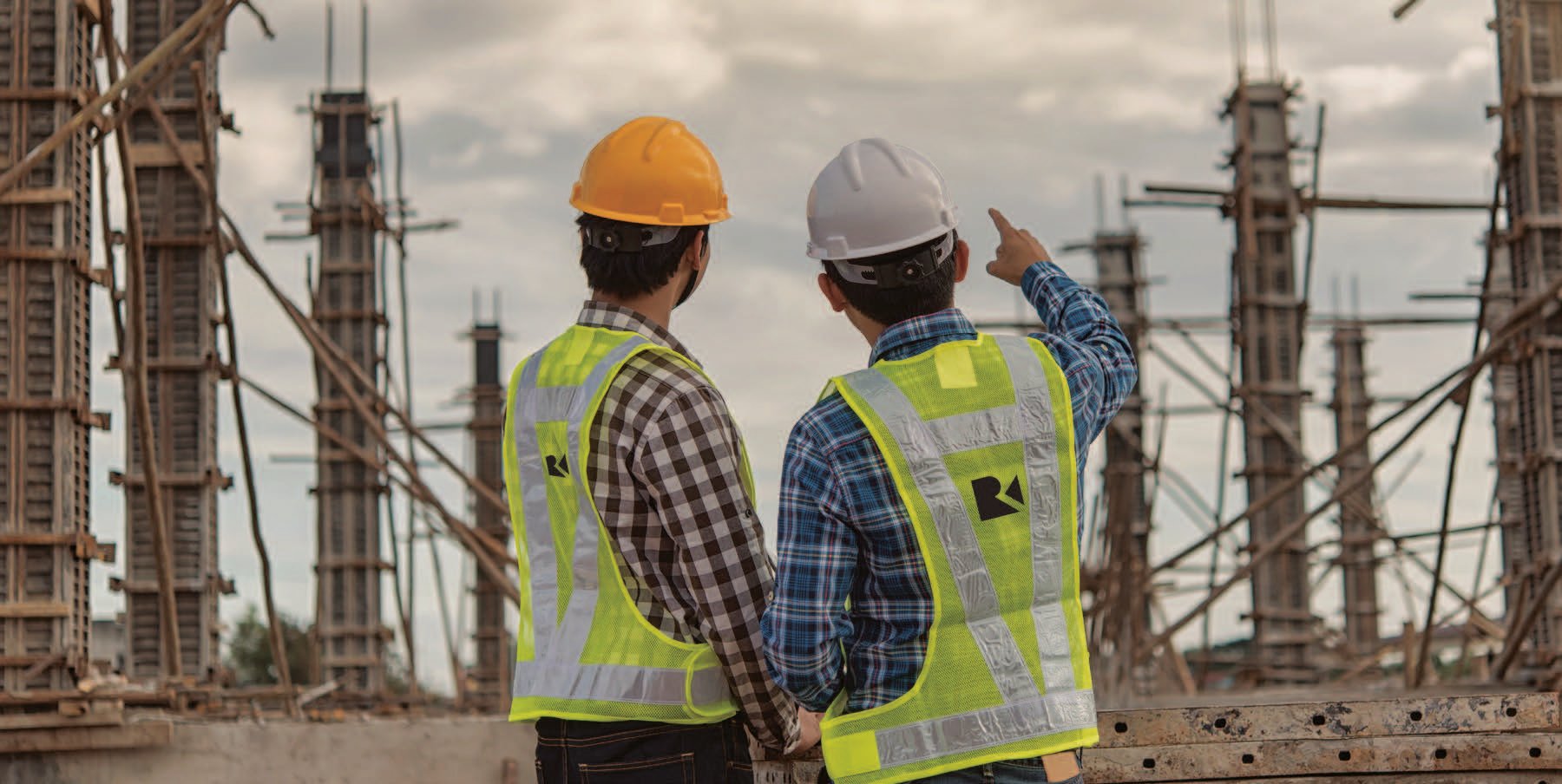 Kiwa Raba engineers in safety gear discussing building project on site with scaffolding and cloudy sky background